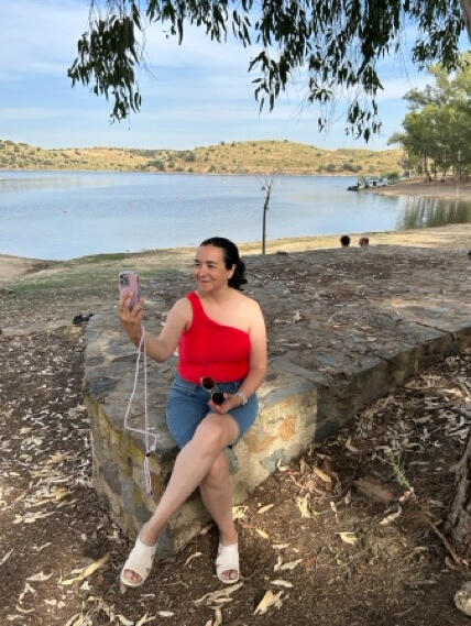 Tisha junto al lago Tisha en bañador con su móvil sentada bajo un eucalipto junto a un embalse extremeño